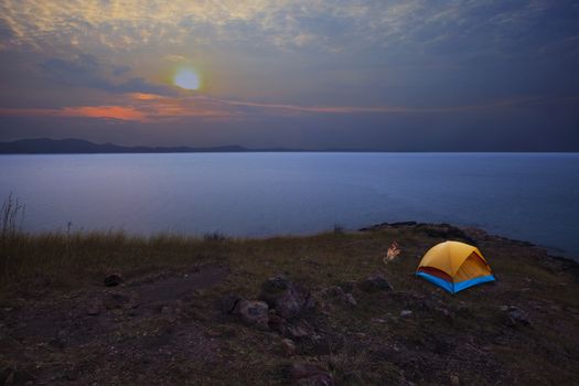 camping tent on rock mountain with sun rising on dramatic sky
