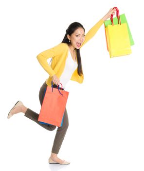 Happy young Asian female shopper running, hands outstretched holding shopping bags and smiling, full length isolated standing on white background.
