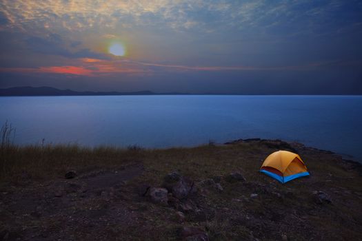 caping tent on mountain with sea coast infront and sun set on dramatic sky