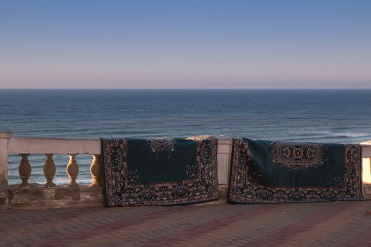 Like after a magic carpet ride, carpets getting dry hanging on the fence. Atlantic ocean in the background. City Sidi Ifni, Morocco.