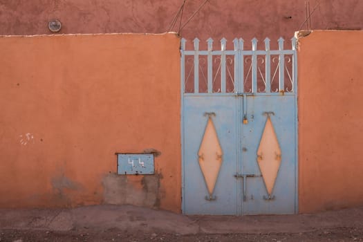 Orange fence with an enlightened blue iron gate. Photo taken in Morocco.