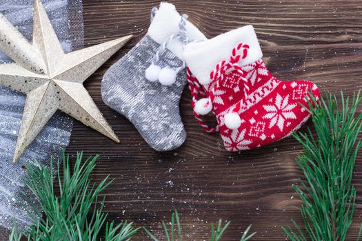 Christmas composition of two knitted socks and xmas tree branches and star ornament on wooden background