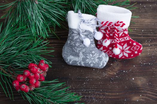 Christmas composition of two knitted socks, rowan berries and xmas tree branches on wooden background