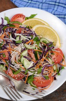 Salad of white and blue chopped cabbage, carrots, cucumber, tomato dressed with oil, lemon, sesame