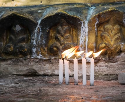 Five candles burning at dawn in front of a golden stupa at the Shwedagon Pagoda in Yangon, Myanmar. Shallow depth of field with the candles in focus.