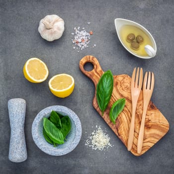 The ingredients for homemade pesto sauce : basil, parmesan cheese ,garlic, olive oil , lemon and himalayan salt over dark concrete background.