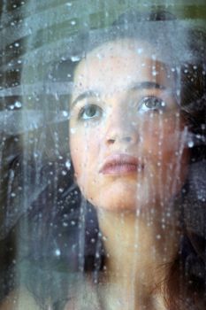 Woman with sad smile behind a wet window