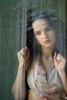 Woman with sad smile behind a wet window