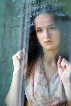 Woman with sad smile behind a wet window