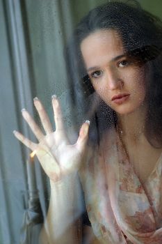 Woman with sad smile behind a wet window