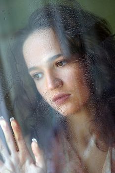 Woman with sad smile behind a wet window