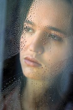 Woman with sad smile behind a wet window