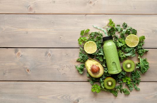 Green smoothie beverage in a bottle over a wooden table with space 