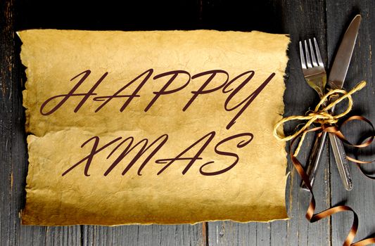 Fork and knife tied with satin ribbon with a blank piece of scroll paper with happy xmas greeting