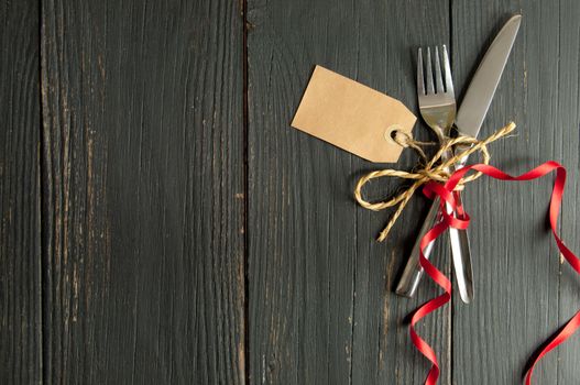 Fork and knife tied together on a wooden table background with tag