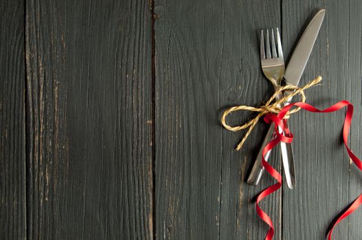 Fork and knife tied together on a wooden table with space