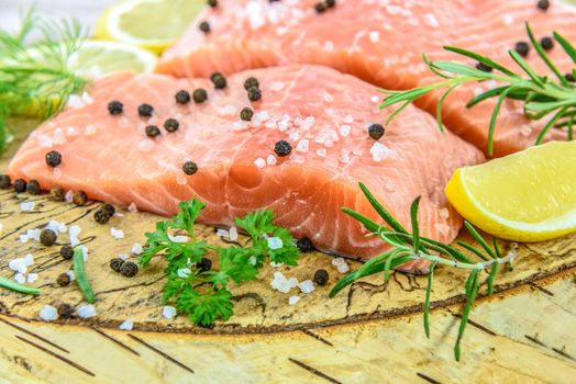 Fresh salmon steak on wooden birch stump pickled lemon, pepper, sea salt, rosemary, parsley, dill