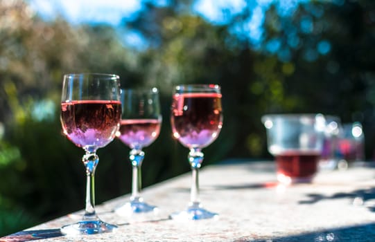 Pink wine in stemmed glasses on a table in a garden in a sunny day