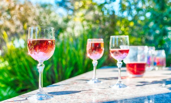 Pink wine in stemmed glasses on a table in a garden in a sunny day