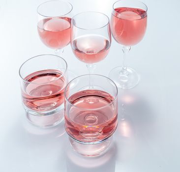 Rosè wine in stemmed glasses on white background with reflection