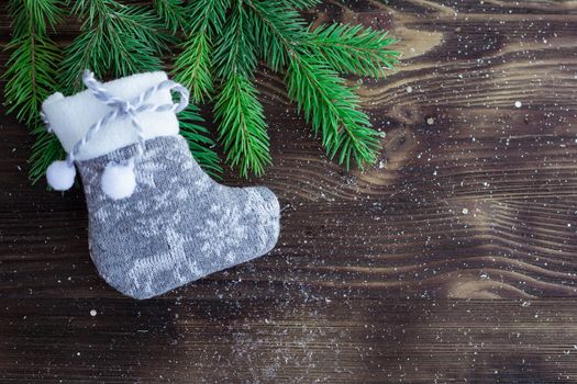 Christmas and New Year holiday composition of green fir tree branches and grey knitted stocking on brown wooden background with copy-space for text