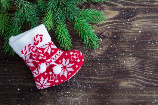 Christmas and New Year holiday composition of green fir tree branches and red knitted stocking on brown wooden background with copy-space for text