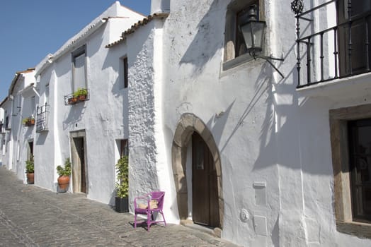 typical street in monsaraz with white houses and pink chair anf flowers in the town
