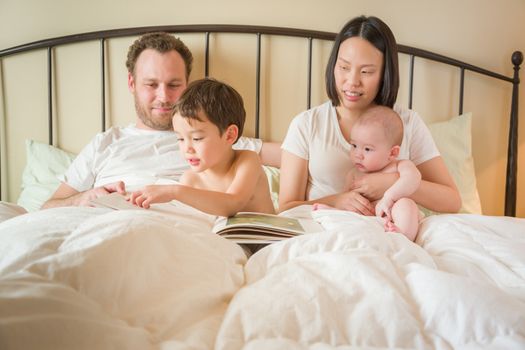 Young Mixed Race Chinese and Caucasian Baby Boys Reading a Book In Bed with Their Father and Mother.