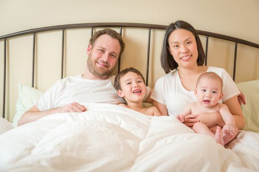 Young Mixed Race Chinese and Caucasian Baby Boys Laying In Bed with Their Father and Mother.