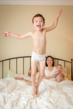 Young Mixed Race Chinese and Caucasian Boy Jumping In Bed with His Family.