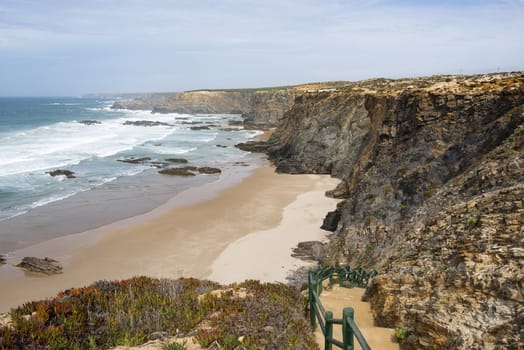 green staircase to the beach and wild ocean splash water to the rocks of the west coast of Portugal