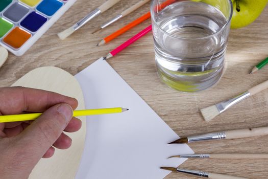 The artist’s hand drawing a paint, brushes and pencils. Art background