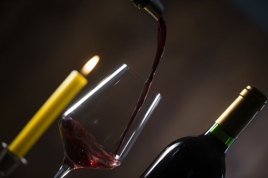 Pouring red wine into wineglass from green bottle, brown background