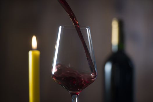 Pouring red wine into wineglass from green bottle, brown background