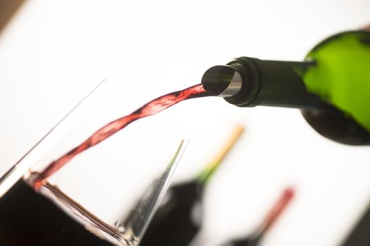 Pouring red wine into wineglass from green bottle, white background