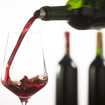 Pouring red wine into wineglass from green bottle, white background