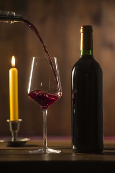 Pouring red wine into wineglass from green bottle, brown background