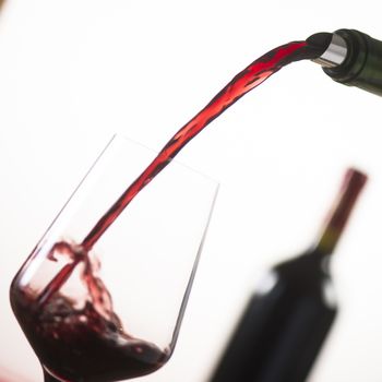 Pouring red wine into wineglass from green bottle, white background