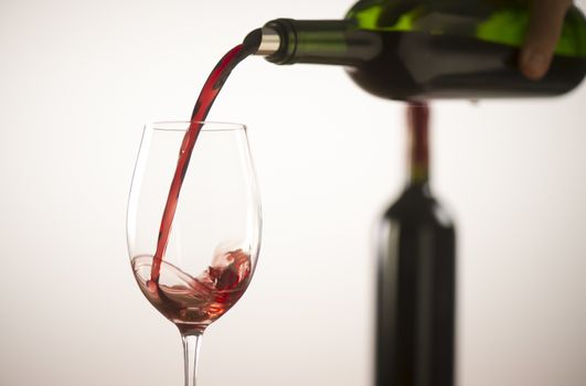 Pouring red wine into wineglass from green bottle, white background