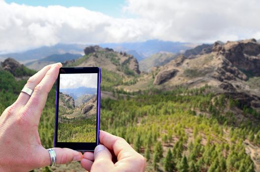 View over the mobile phone display during taking a picture of mountains in Gran Canaria. Holding the mobile phone in hands and taking a photo. Focused on mobile phone screen. 