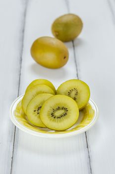 golden kiwi fruit and sliced on dish over white wooden background