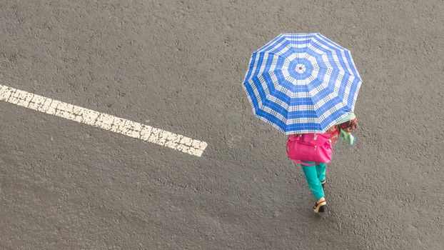 Top view of a woman holding an umbrella and an pink purse crossing the street