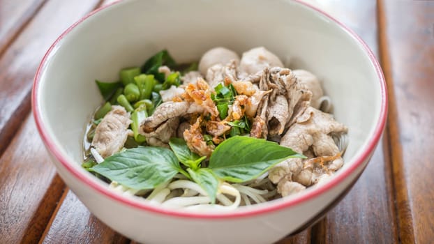 Asian white noodles with pork and vegetables in bowl over wooden background