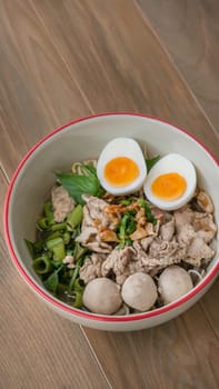 Asian white noodles with pork and vegetables in bowl over wooden background