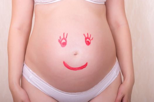 Face drawn in lipstick on a stomach of the pregnant woman