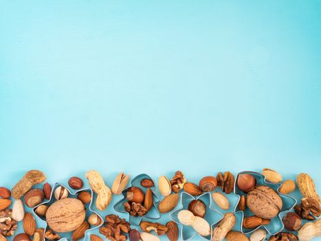 mixed nuts with christmas cookie cutters on blue background with copy space. Top view o flat lay. Toned image