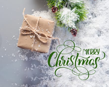 box of kraft paper and fir branch in the snow with text Merry Christmas. Lettering calligraphy.
