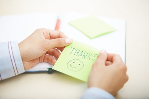 Hands of woman holding sticky note with Thanks text