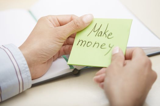 Hands of businessperson holding adhesive note with Make money text