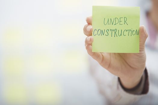Woman holding sticky note with Under construction text